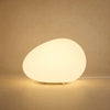Lampe à poser galet lumineux Sassolia allumée en blanc chaud sur fond minéral sable | Delvanie