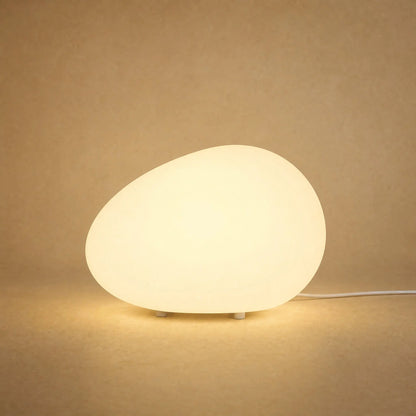 Lampe à poser galet lumineux Sassolia allumée en blanc chaud sur fond minéral sable | Delvanie