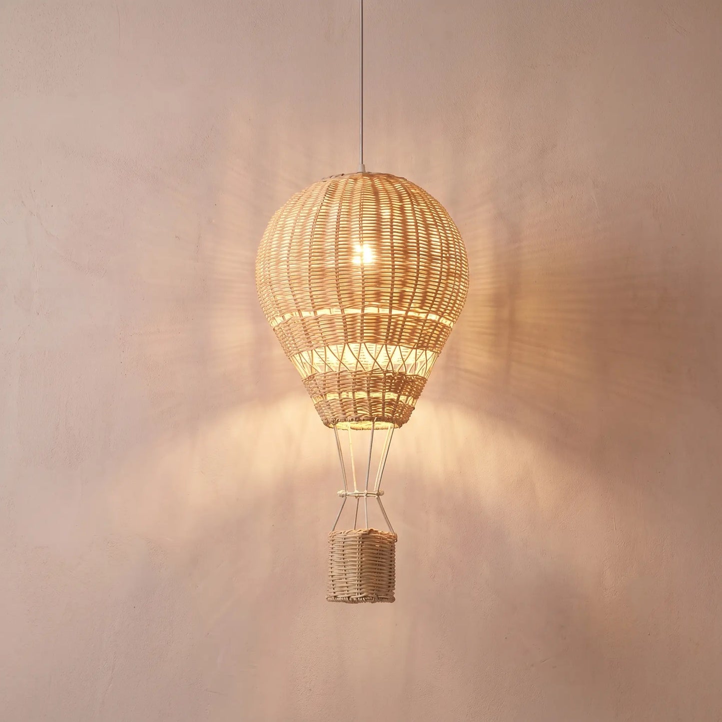 Suspension enfant rotin montgolfière LED dimmable Ballora, allumée sur fond rose-beige