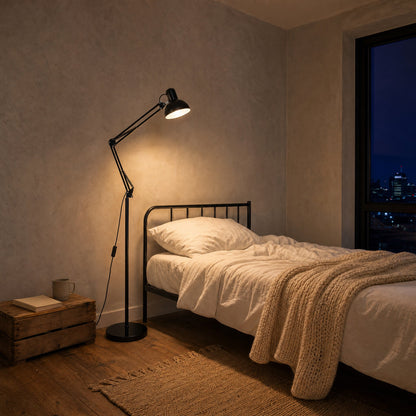 Lampadaire liseuse noir allumé au-dessus d'un lit dans un petit studio le soir | Delvanie