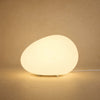 Lampe à poser galet lumineux Sassolia allumée en blanc chaud sur fond minéral sable | Delvanie