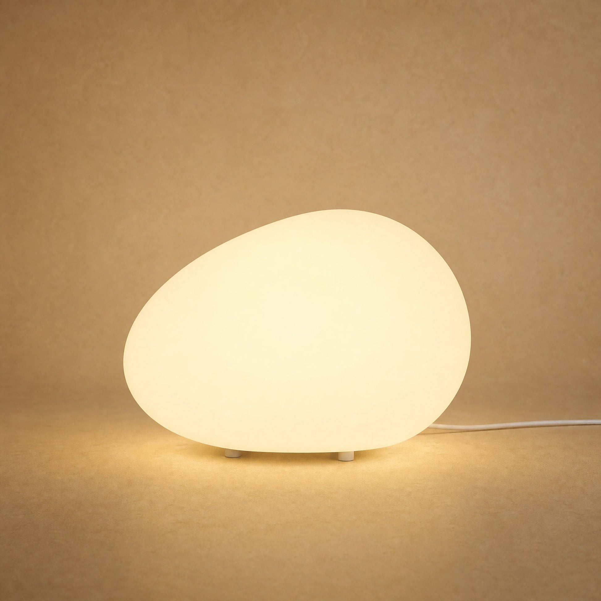 Lampe à poser galet lumineux Sassolia allumée en blanc chaud sur fond minéral sable | Delvanie